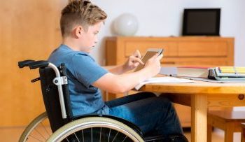 мальчик в инвалидном кресле за столом с планшетом